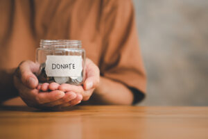 Person holding a glass jar filled with coins labeled Donate representing charitable giving and planned donations in retirement